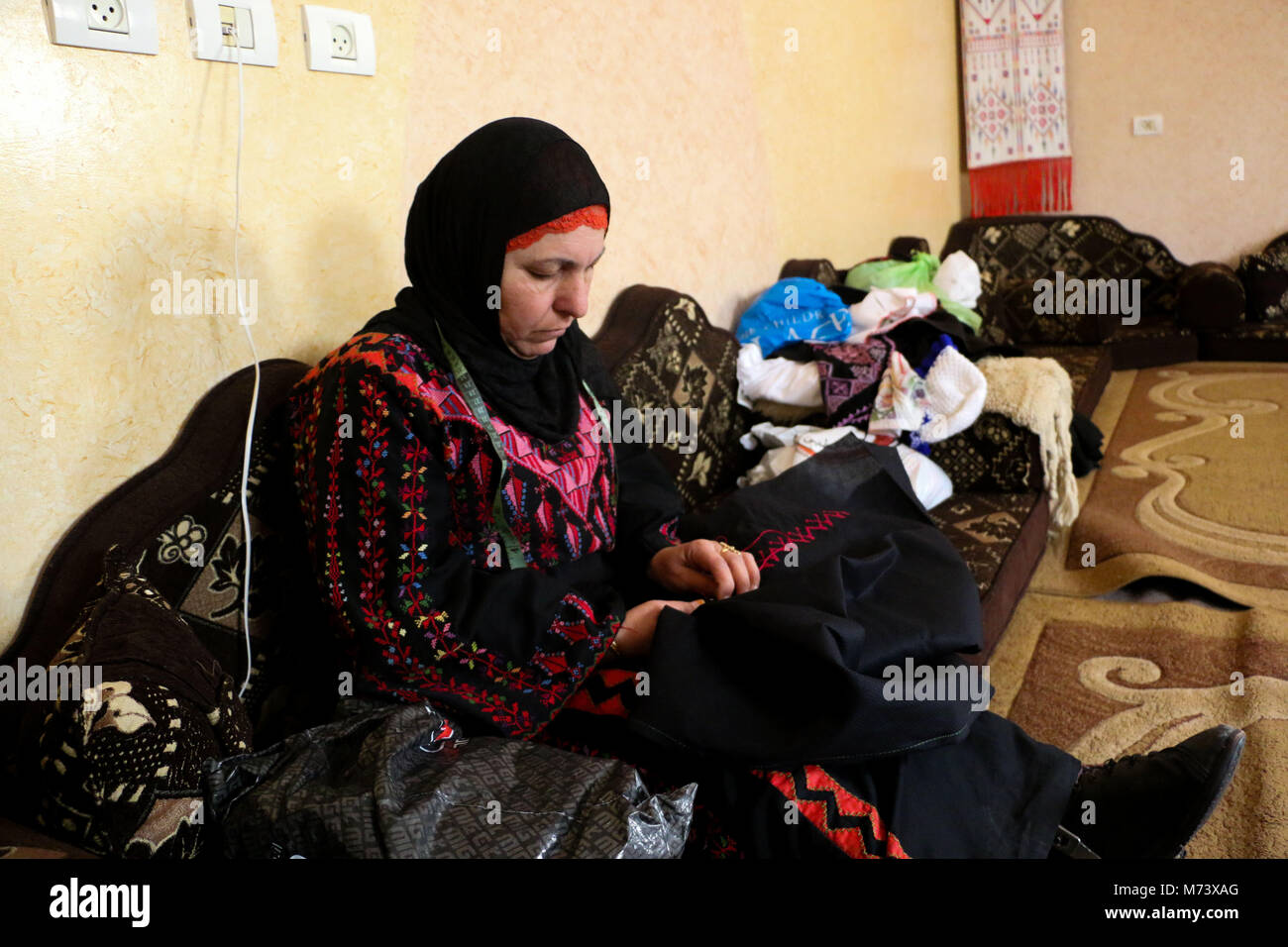 March 8, 2018 - Fifty years old Jihad Zuhdi Awad, from al-Bureij Palestinian refugee camp in the central Gaza Strip, has been embroidering for 41 years in spite of being affecting from a disability in her left foot as a result of a medical error. Her lounge is scattered with hand-made embroidered items including embroidered dresses, shawls, picture frames, bags, and pieces hanging on walls. Hand embroidery is a highly respected art in Palestine and it is an integral part of the nation's heritage Credit: Ahmad Hasaballah/ImagesLive/ZUMA Wire/Alamy Live News Stock Photo