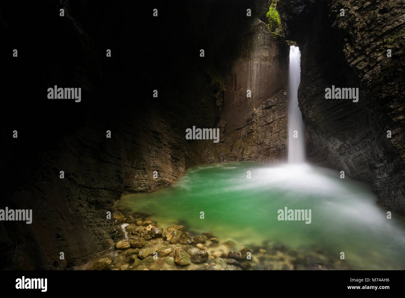 Hidden Kozjak waterfall streams out of layered, mossy rocks in a deep gorge, crystal clear pool. Stock Photo