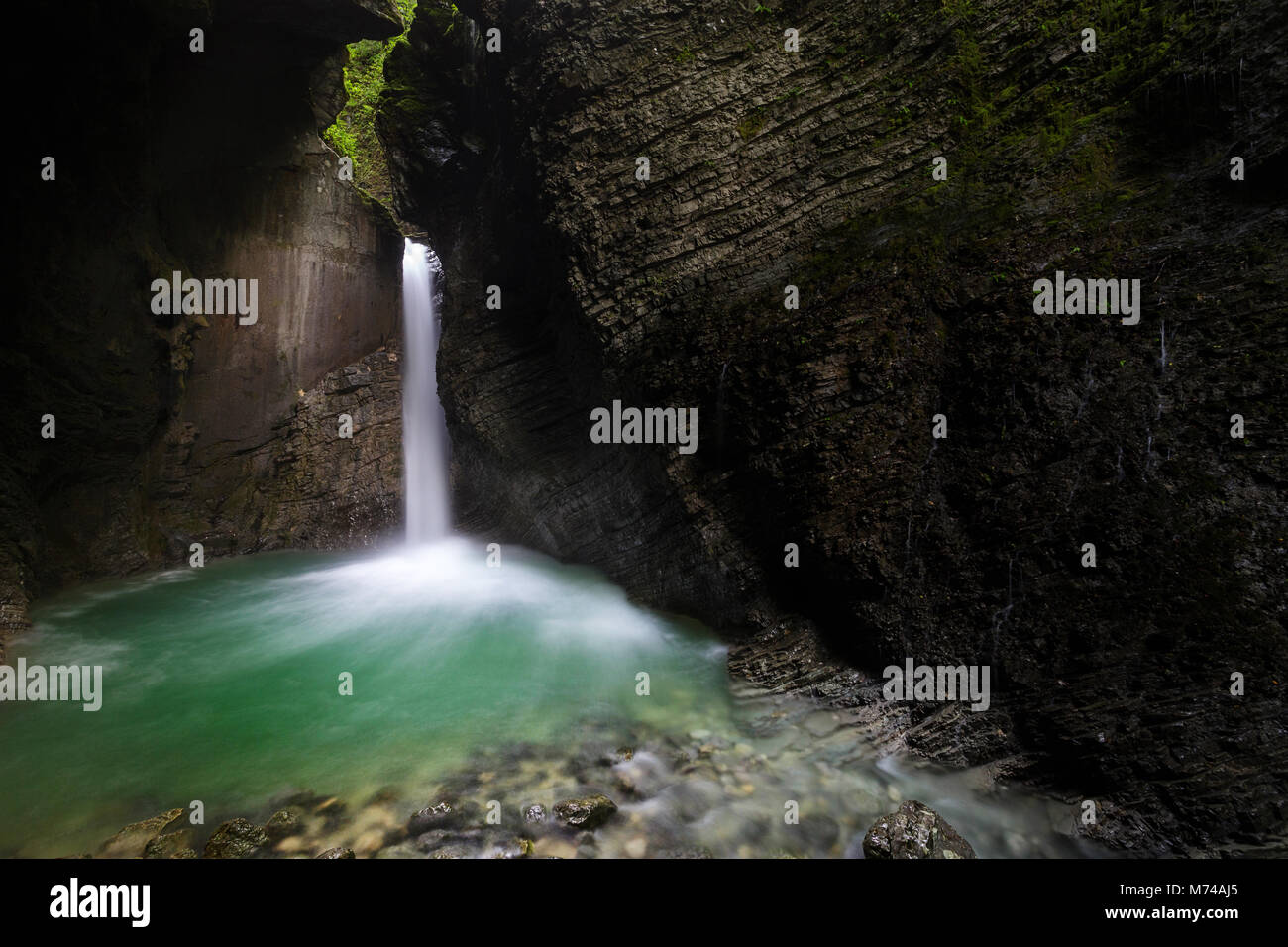 Hidden Kozjak waterfall streams out of layered, mossy rocks in a deep gorge, crystal clear pool. Stock Photo