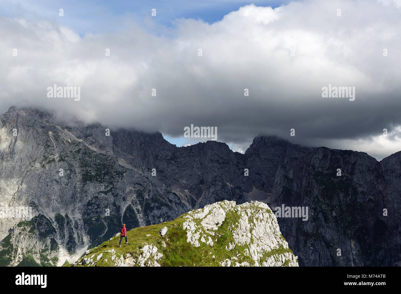 Woman in red jacket hiking on steep slopes, Mangart saddle, Julian alps, Slovenia Stock Photo