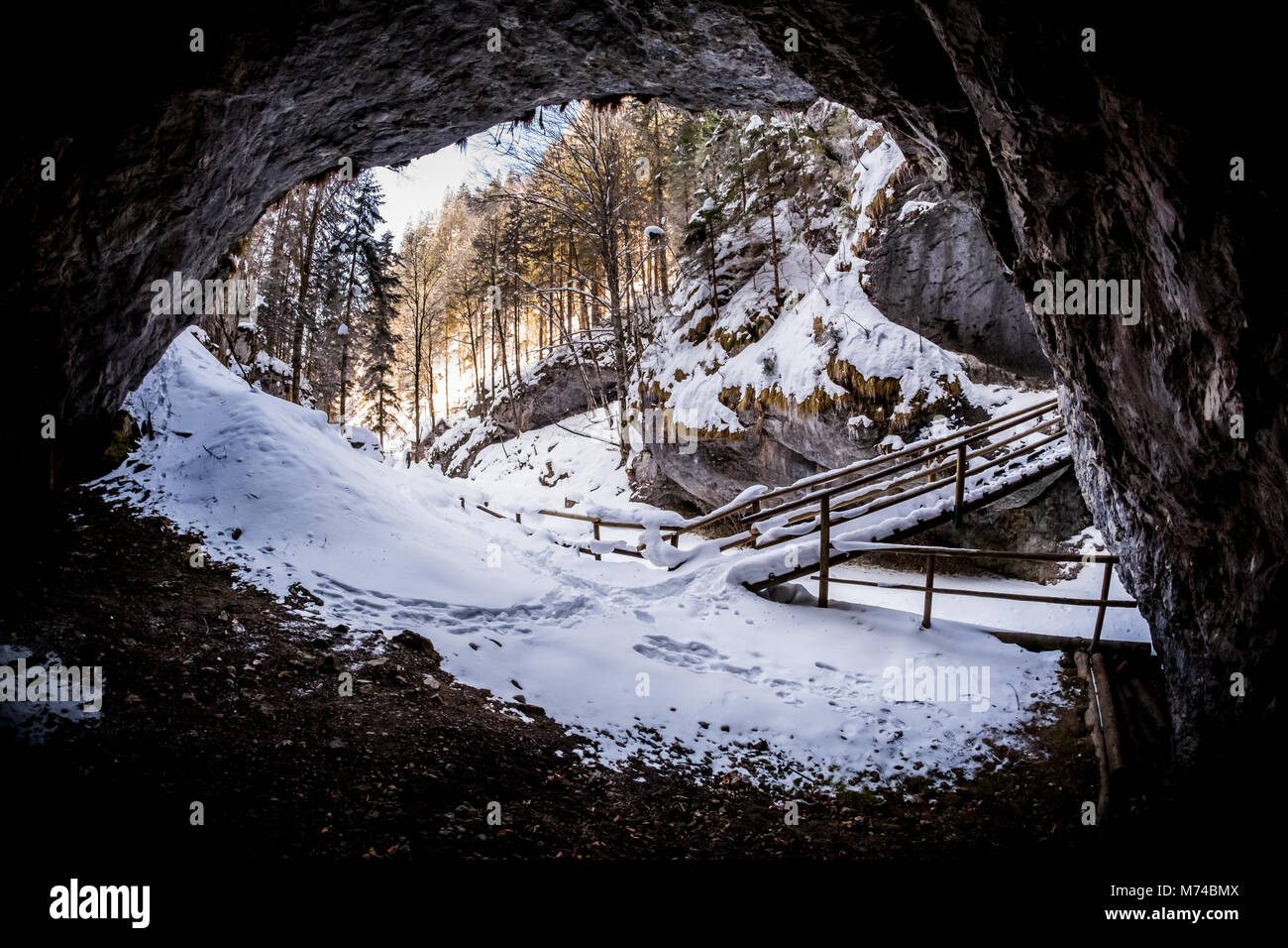View from dark cave to snow covered gorge Baerenschuetzklamm with forest and wooden bridge in winter Stock Photo