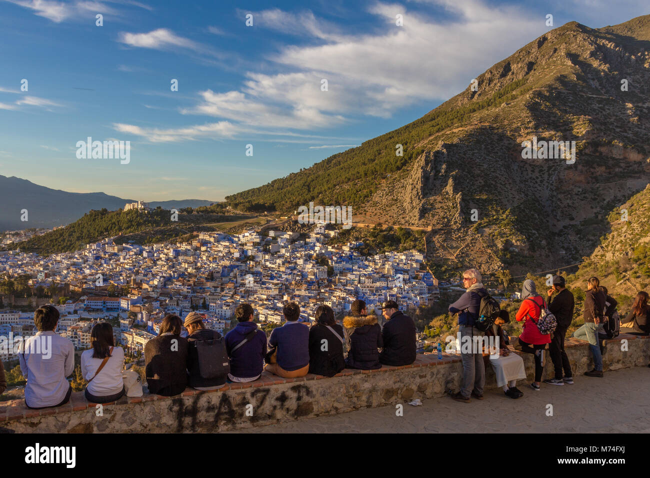 A row of tourists watch sunset over the rooftops of Chefchaouen from the Spanish Mosque, northwest Morocco. Stock Photo