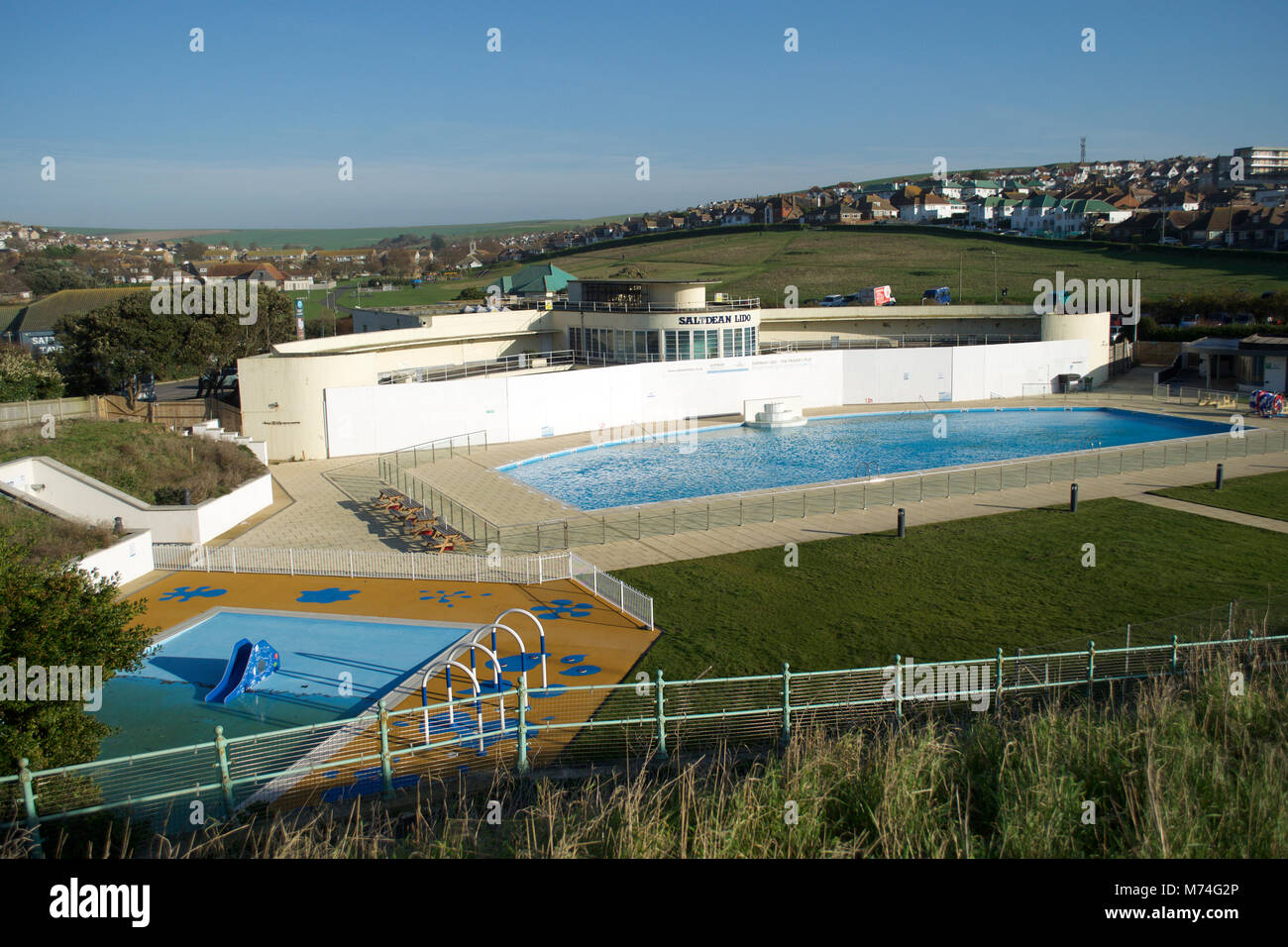 Saltdean Lido Art Deco refurbished outdoor kids swimming pool East Sussex South Downs green hills morning sunshine blue water Stock Photo