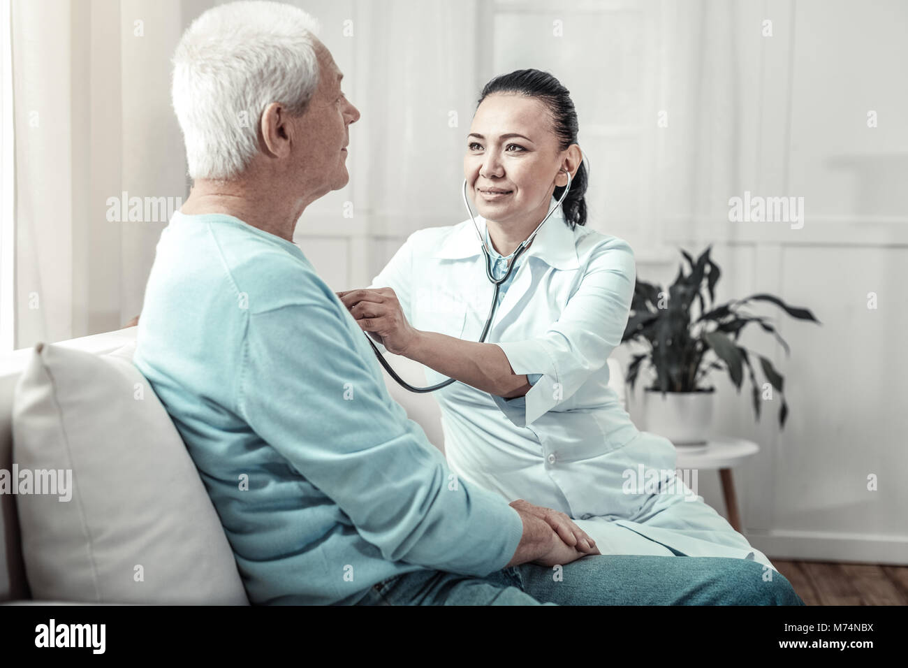 Young skilled nurse sitting and listening to the patients lungs. Stock Photo