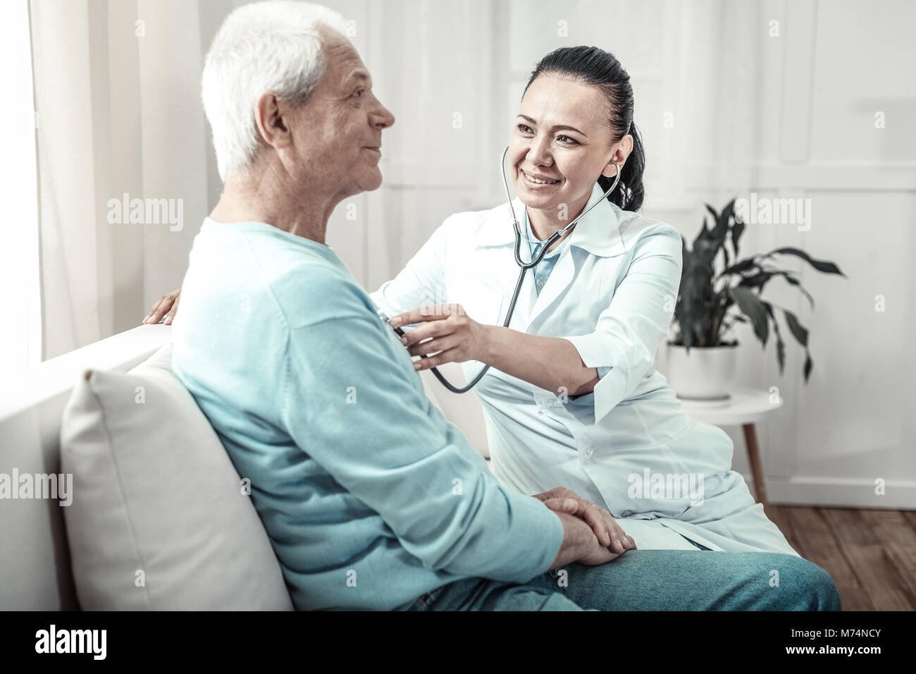 Pleasant kind nurse using her stethoscope and smiling. Stock Photo