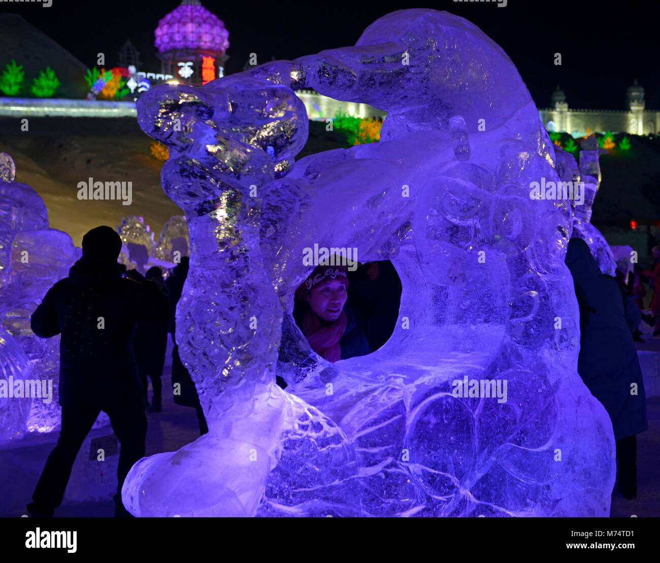 A woman has her picture taken through an ice sculpture at the 2018 Harbin International Ice and Snow Sculpture Festival Stock Photo
