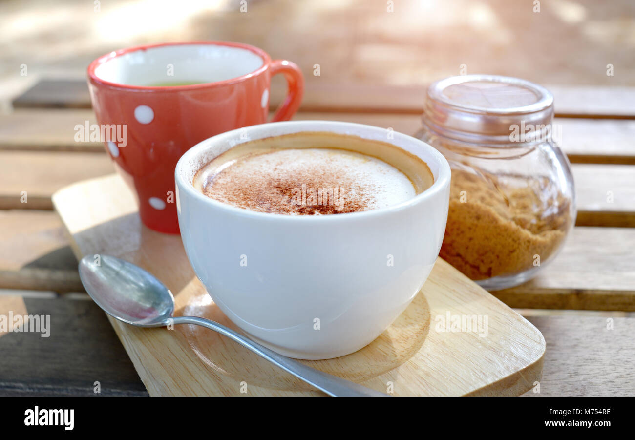 Hot cappuccino coffee on the  wooden table style in outdoor morning low and soft lighting. Stock Photo