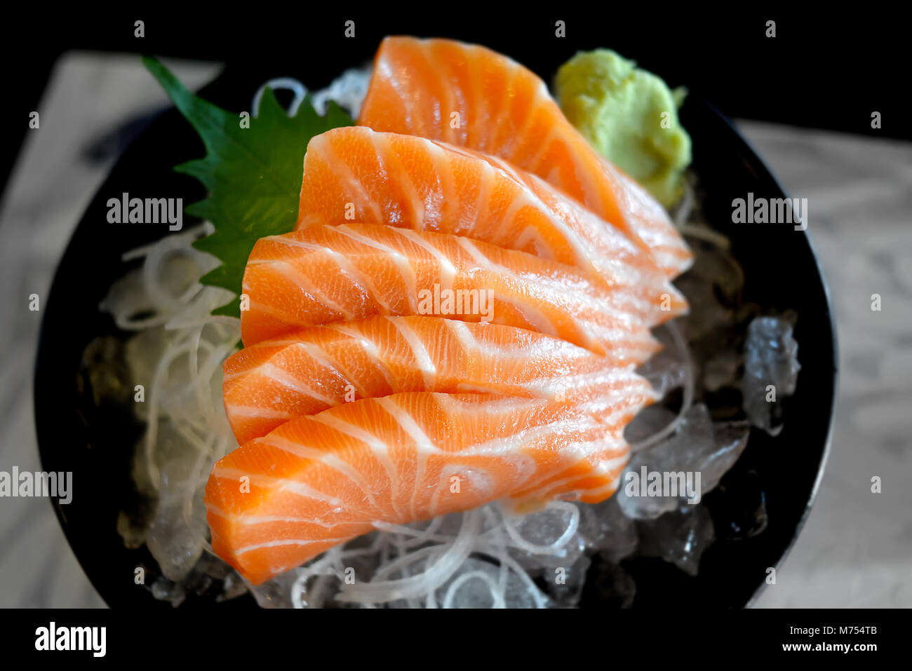 Raw salmon slice or salmon sashimi in Japanese style fresh serve on ice with fresh wasabi photo in  indoor low lighting. Stock Photo