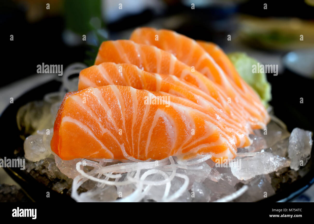 Raw salmon slice or salmon sashimi in Japanese style fresh serve on ice with fresh wasabi photo in  indoor low lighting. Stock Photo