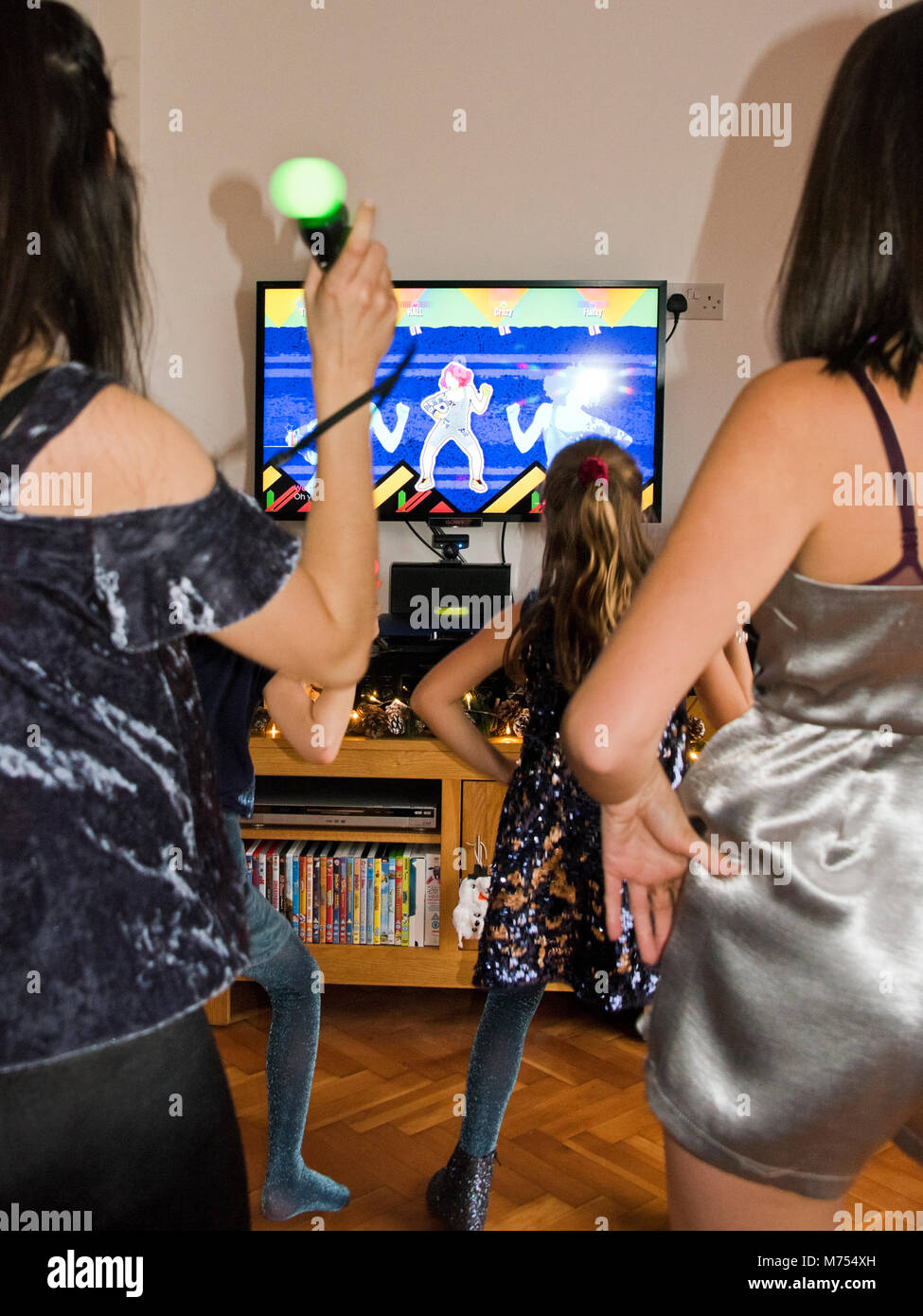 Vertical portrait of four girls dancing and singing together on their games console. Stock Photo