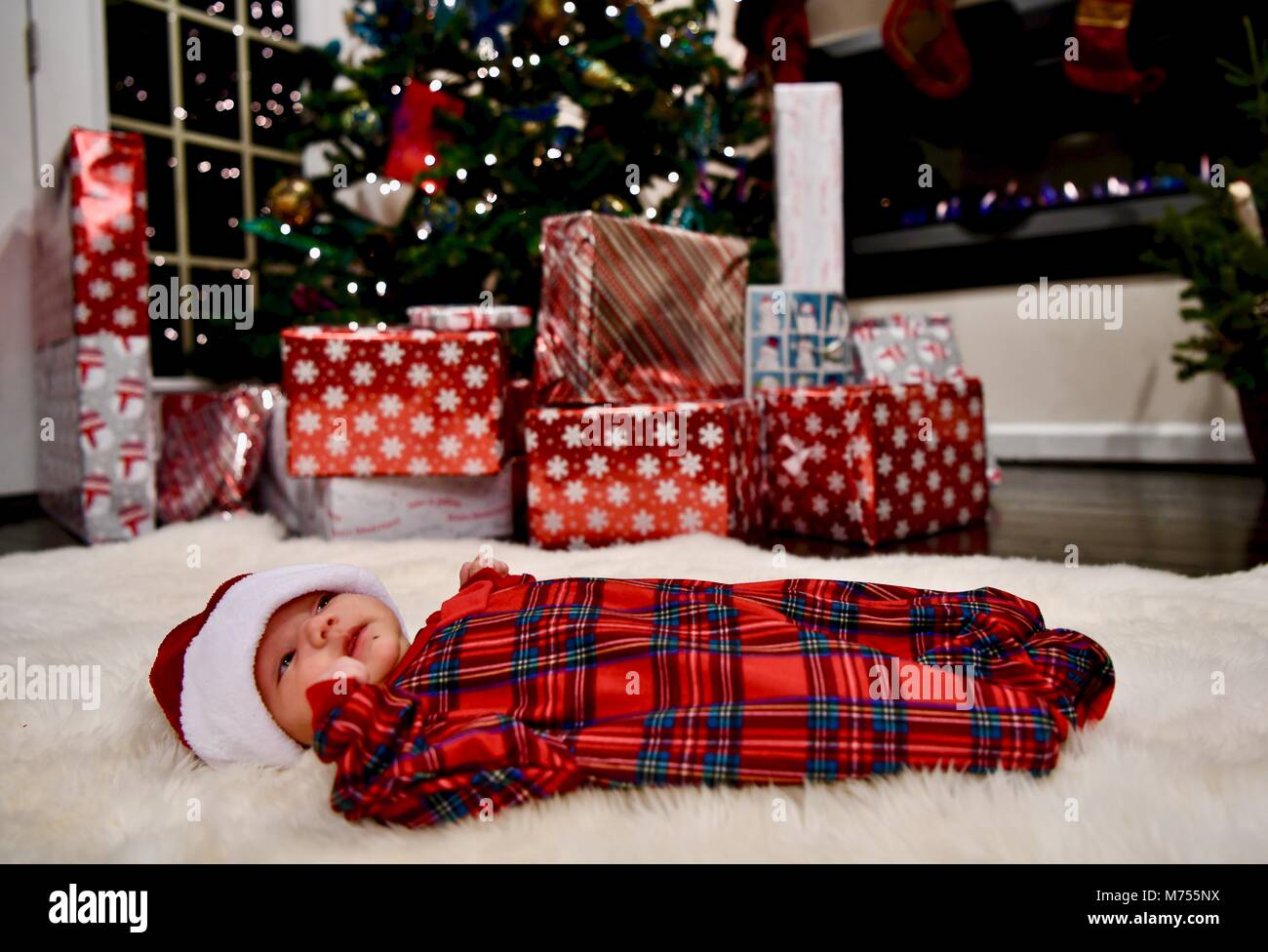 Newborn baby aged 1-4 months dressed up on Christmas eve laying next to a Christmas tree with presents Stock Photo