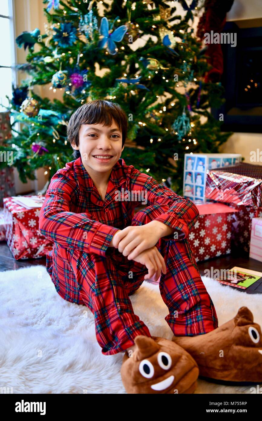 Young teen aged 10-14 on Christmas morning next to the Christmas tree with presents Stock Photo