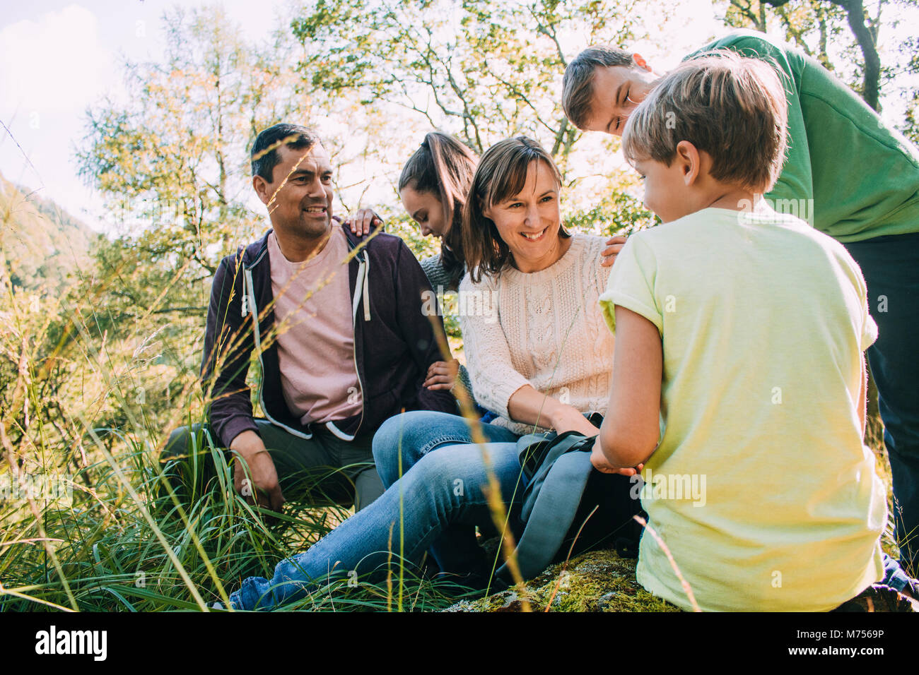 Happy family are taking a break from their hike to eat their packed lunches. Stock Photo