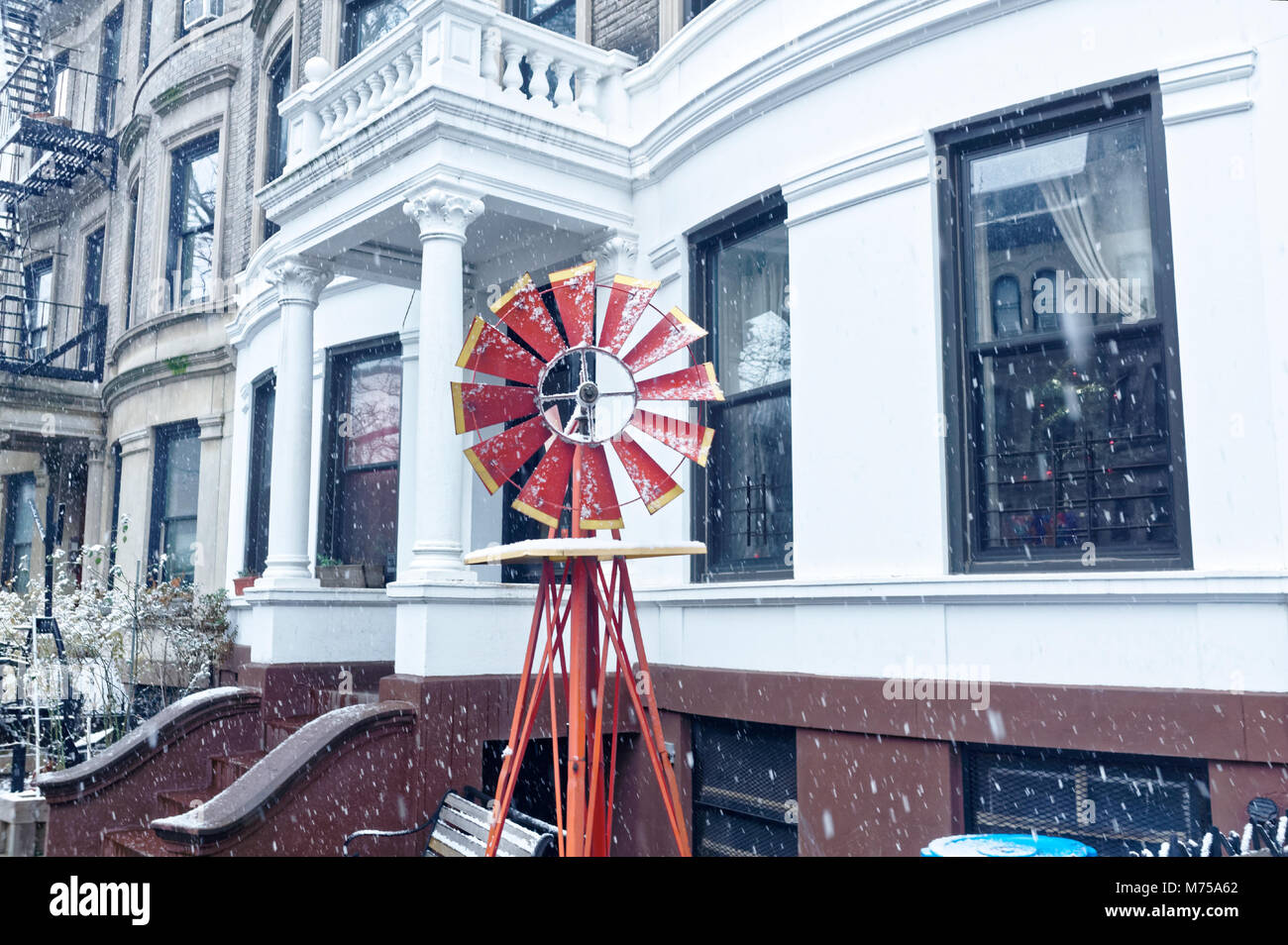 Small red decorative windmill in an urban neighborhood during a light snowfall. Stock Photo