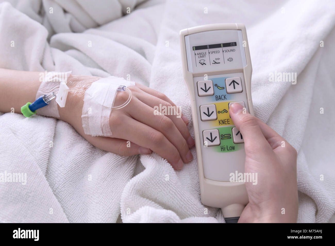 female patient adjust the height of the patient bed by press the button up of automatic patient bed remote control in the room of the hospital. Stock Photo