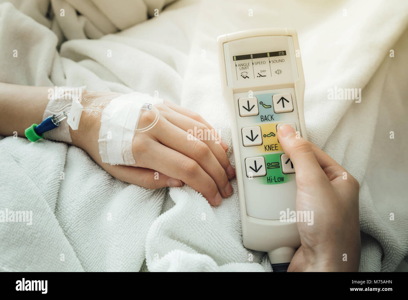 female patient adjust the height of the patient bed by press the button up of automatic patient bed remote control in the room of the hospital. select Stock Photo