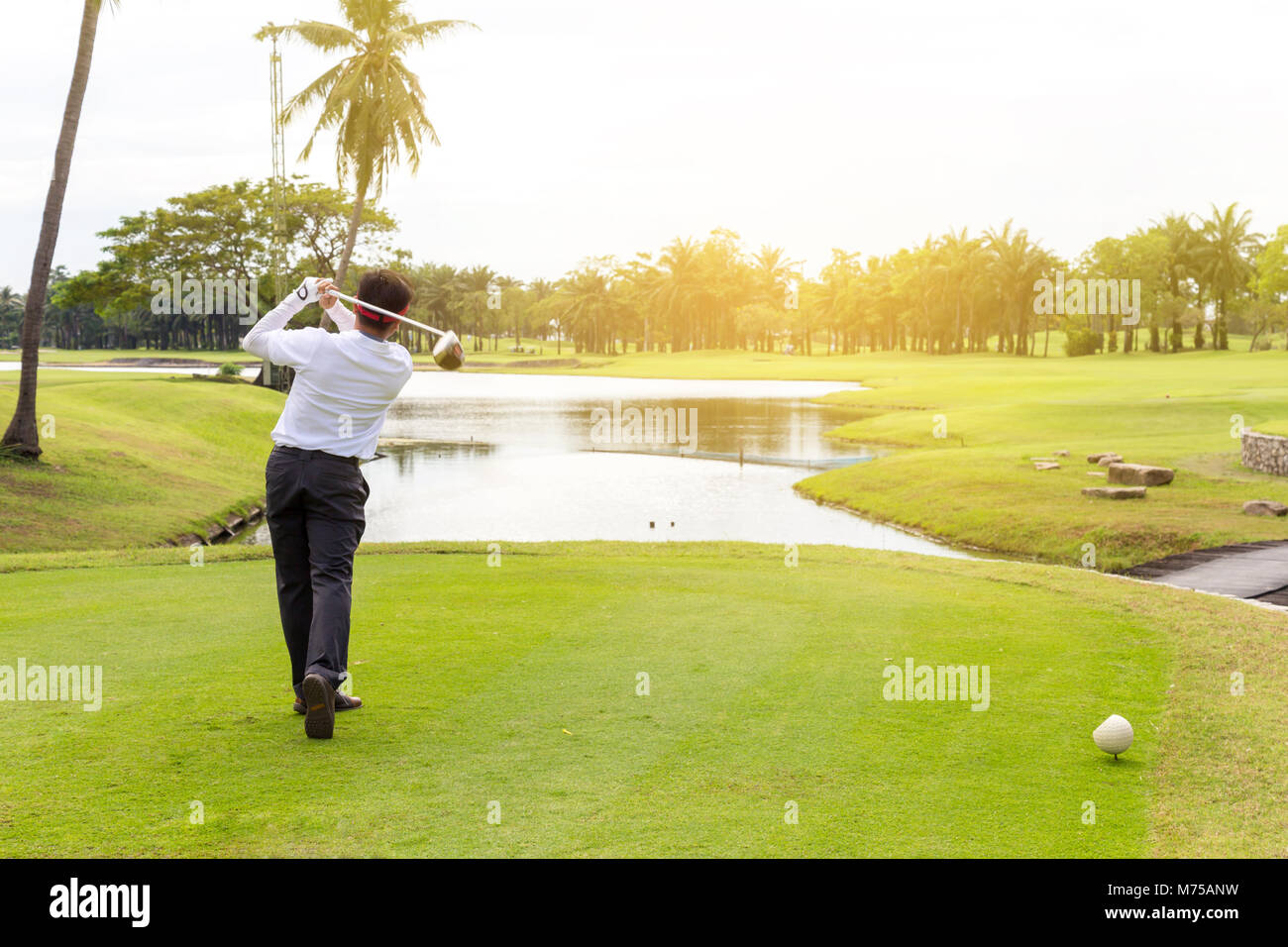 young asian businessman playing golf on the beautiful golf course in the morning with sunbeam at summer time. Stock Photo