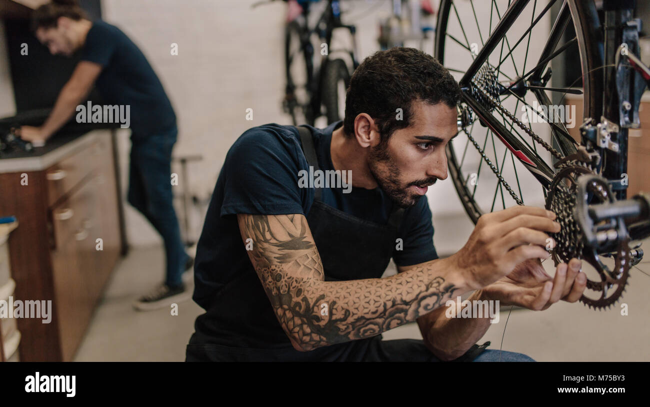 Man fixing a bicycle in a repair shop. Worker fixing bicycle gear and chain in workshop Stock Photo - Alamy