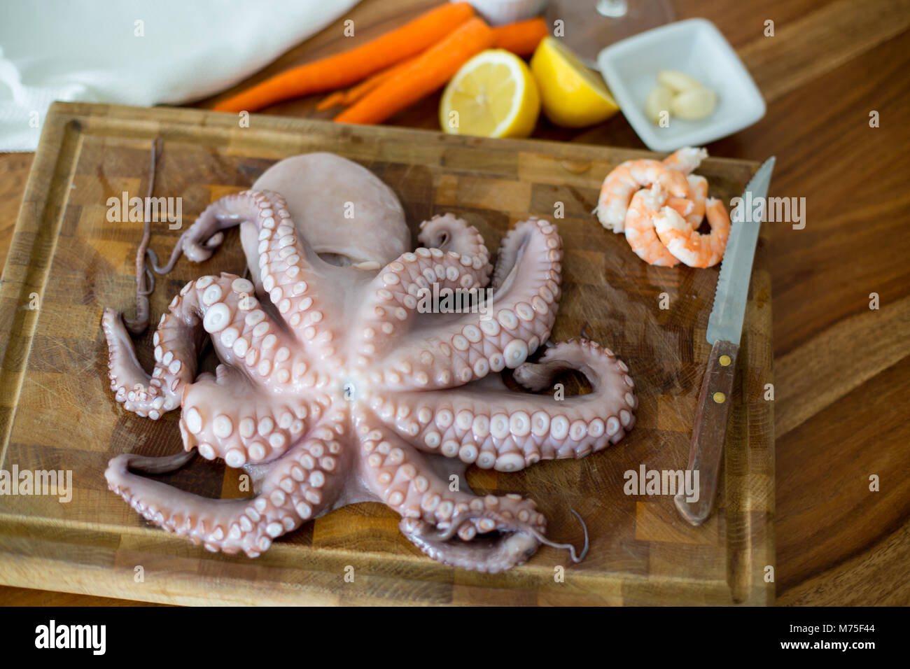 Fresh octopus on chopping board with lemon,white wine and pepper on wooden rustic table Stock Photo