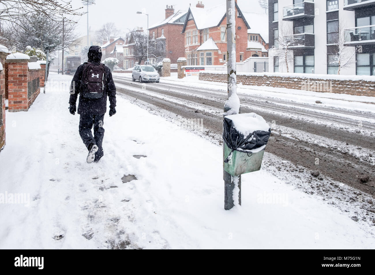 Cold Winter day. A person walking along a pavement with falling snow and a road with snow and slush, West Bridgford, Nottinghamshire, England, UK Stock Photo