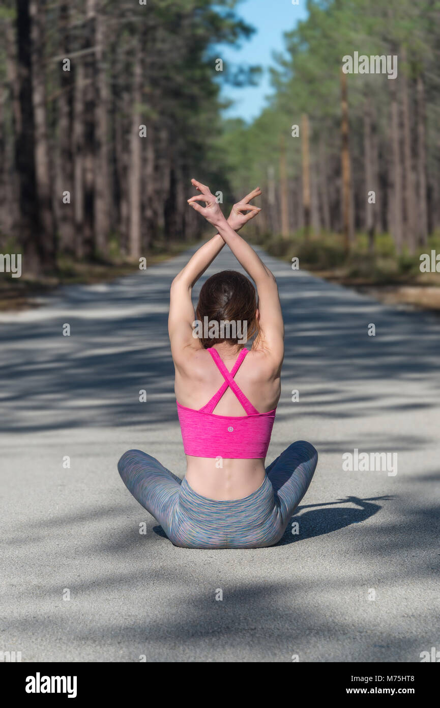 Woman sitting in middle of a straight road through a forest practicing ...
