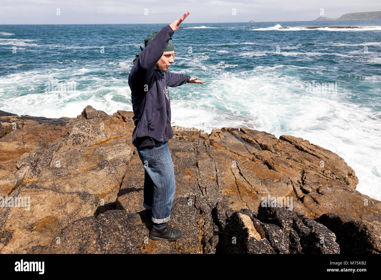 A tourist watching forceful waves hitting rocks in Cornwall on the coast by the Celtic Sea Stock Photo