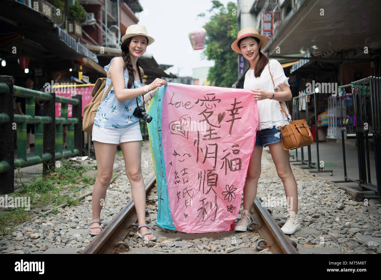 Women write their wishes on the sky lanterns in Chinese. Releasing the lantern on the railway. Translation on sky lanterns text 'hopes of happiness an Stock Photo