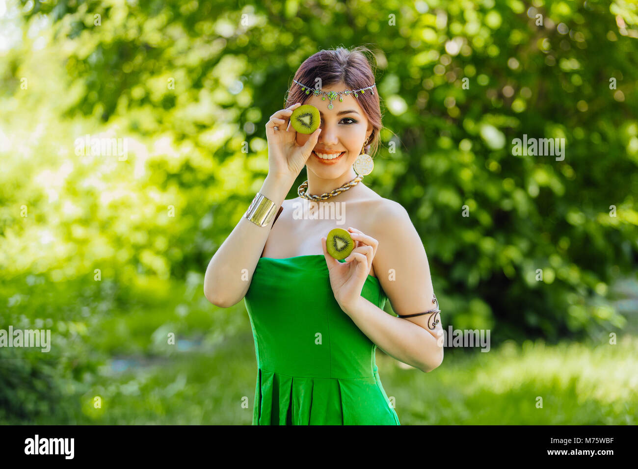 Portrait of a beautiful young asian woman holding two halves of kiwi ...