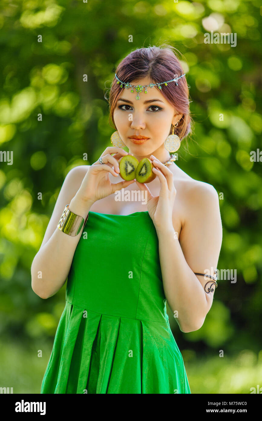 Portrait of a beautiful young asian woman holding two halves of kiwi ...
