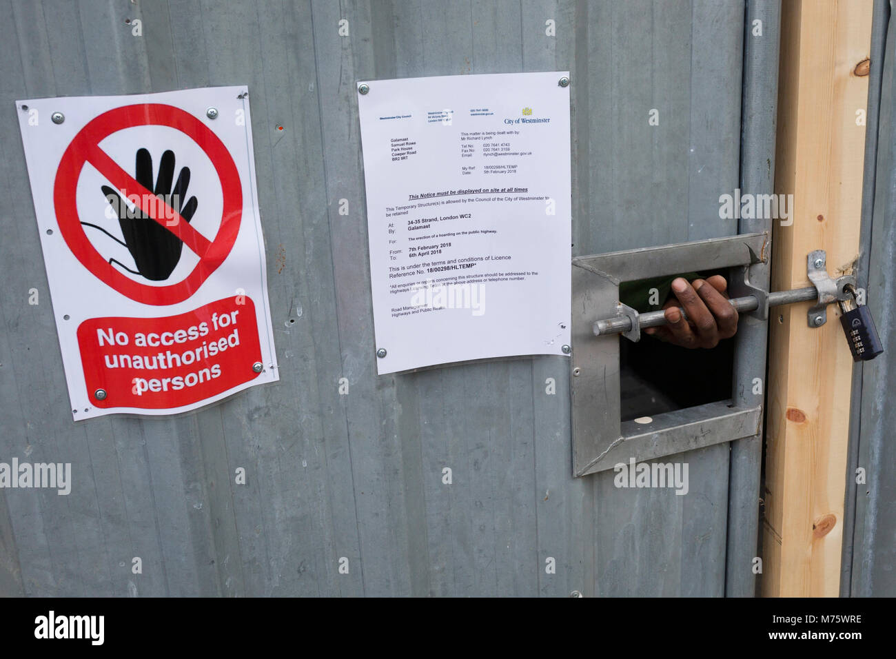 A construction worker's hand feels for the padlock of a locked site door on the Strand, on 5th March 2018, in London, England. Stock Photo