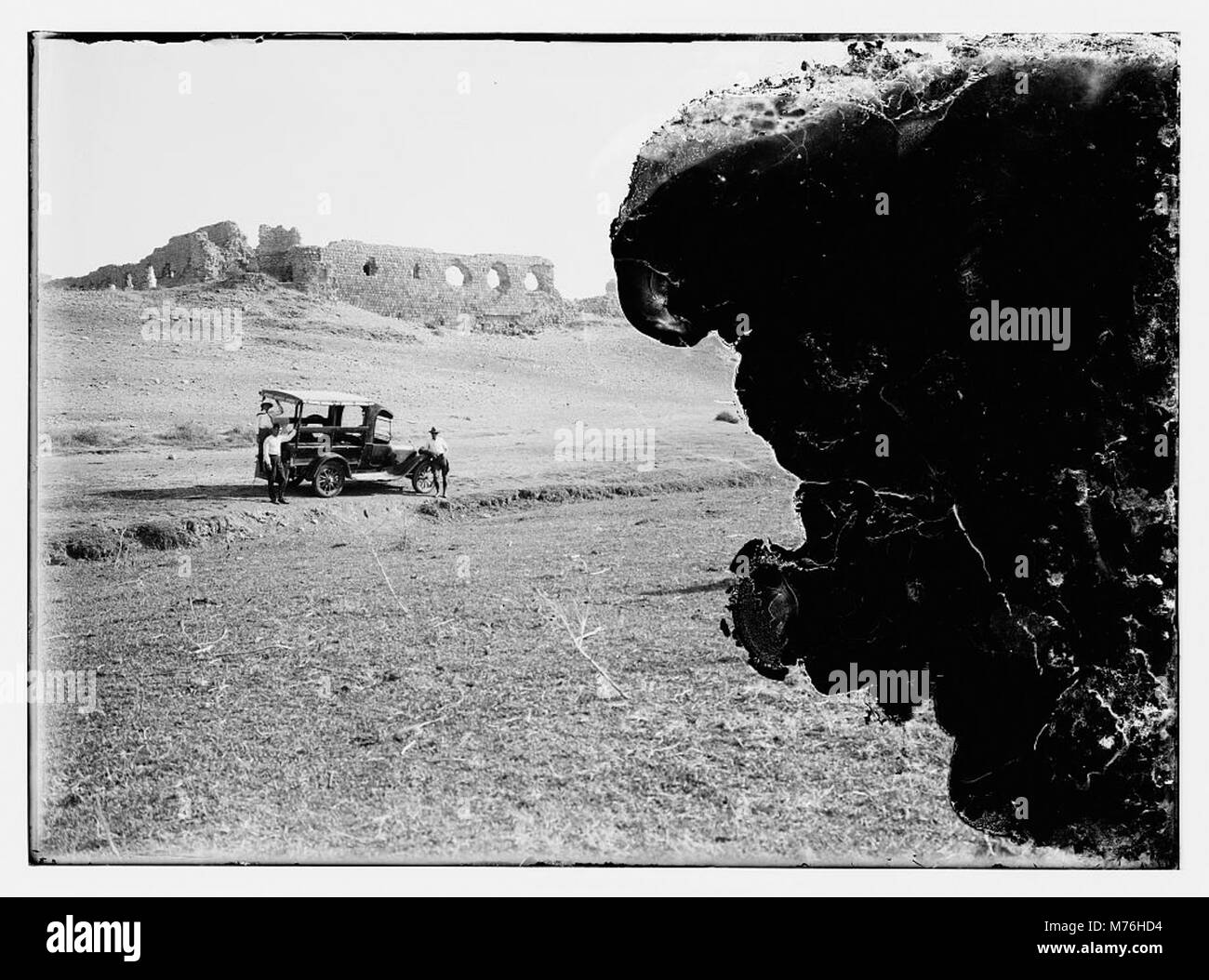 A historical photograph of people in a car near ruins, possibly after a disaster or in an area of archaeological interest. The photo provides insight into the intersection of modern life and historical sites. Stock Photo