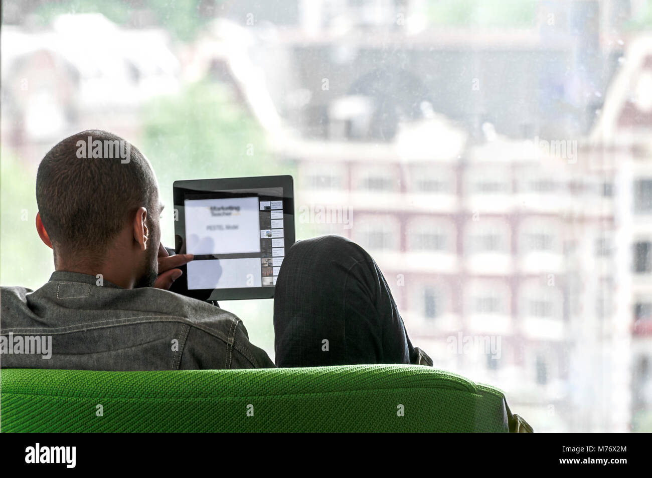 Man Sitting On A Green Bench Looks At A Small Screen Stock Photo