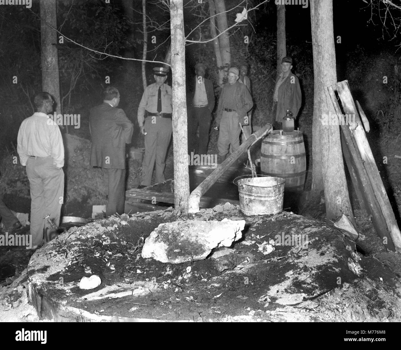 Law enforcement officials investigate the scene of an illegal backwoods moonshine still in rural Georgia, ca. 1955. Stock Photo