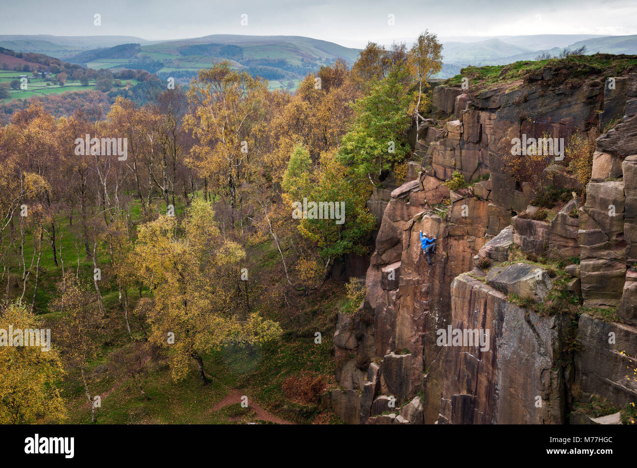 A rock climber ascends a cliff face formed by historic quarrying at Bole hill quarry on an autumn day in the Peak District, Derbyshire, England, UK Stock Photo