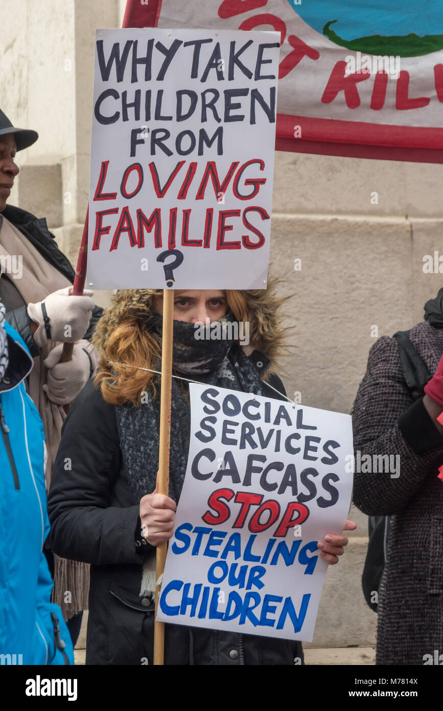 London, UK. 8th March 2018. A woman with a placard 'Why take children form Loving Families' and a poster accusing social services and CAFCAAA of stealing children at the Global Women's Strike mock trial of the Family Courts in an International Women’s Day protest in front of Parliament. Speakers included mothers who have had children unjustly removed and others who read out shocking comments made in court by judges. The UK has the highest rate of adoptions in Europe, almost all without consent of their birth family. In some working class areas, 50% of children are referred to social services a Stock Photo