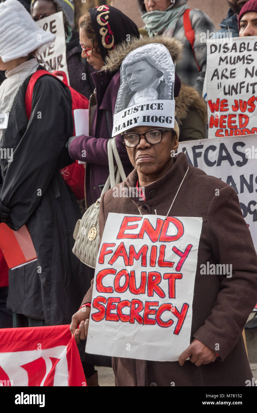London, UK. 8th March 2018. A woman with a picture of Justic Mary Hogg on her head and a poster 'End Family Court Secrecy' at the Global Women's Strike mock trial of the Family Courts in an International Women’s Day protest in front of Parliament. Speakers included mothers who have had children unjustly removed and others who read out shocking comments made in court by judges. The UK has the highest rate of adoptions in Europe, almost all without consent of their birth family. In some working class areas, 50% of children are referred to social services and that families of colour, immigrant an Stock Photo