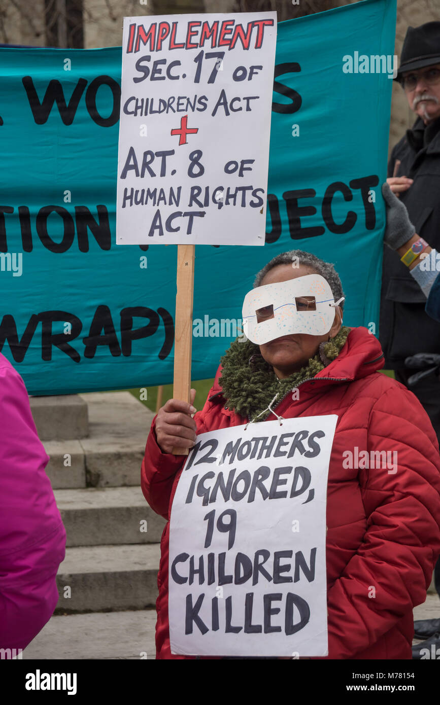 London, UK. 8th March 2018. A masked woman holds a placard and a poster at the Global Women's Strike mock trial of the Family Courts in an International Women’s Day protest in front of Parliament. Speakers included mothers who have had children unjustly removed and others who read out shocking comments made in court by judges. The UK has the highest rate of adoptions in Europe, almost all without consent of their birth family. Credit: Peter Marshall/Alamy Live News Stock Photo
