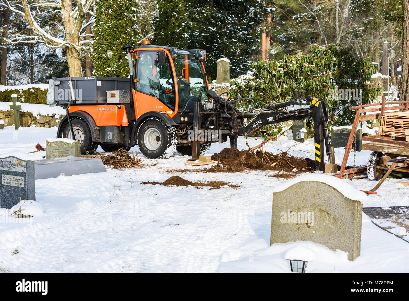 Ronneby, Sweden - March 1, 2018: Documentary of everyday life and environment. Holder C480 tractor used as a grave digger at a cemetery in winter. Roo Stock Photo