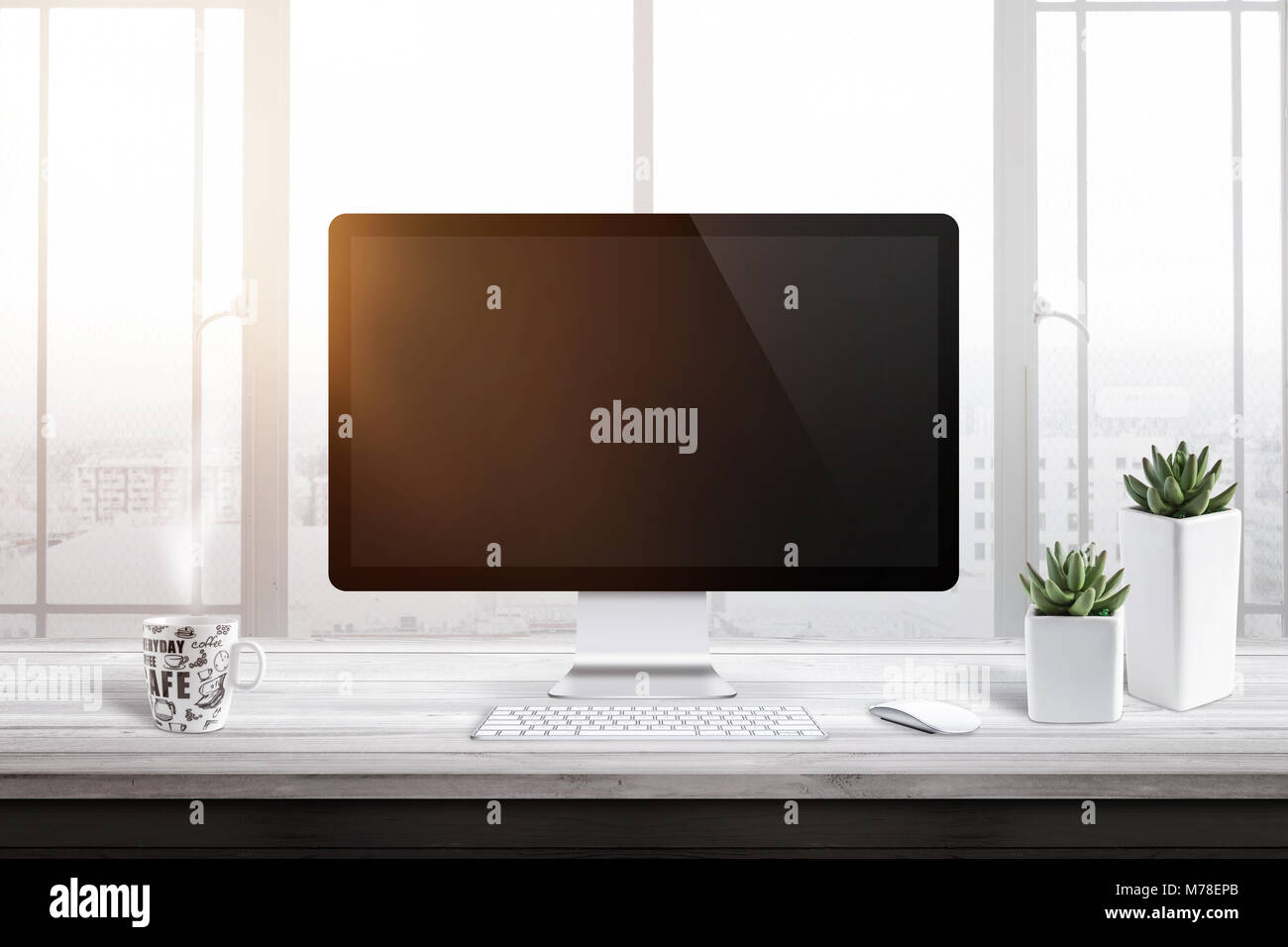 Computer display with blank screen for mockup in office or work room. Window and sun light in background. Cup of coffee and two plants beside. Stock Photo