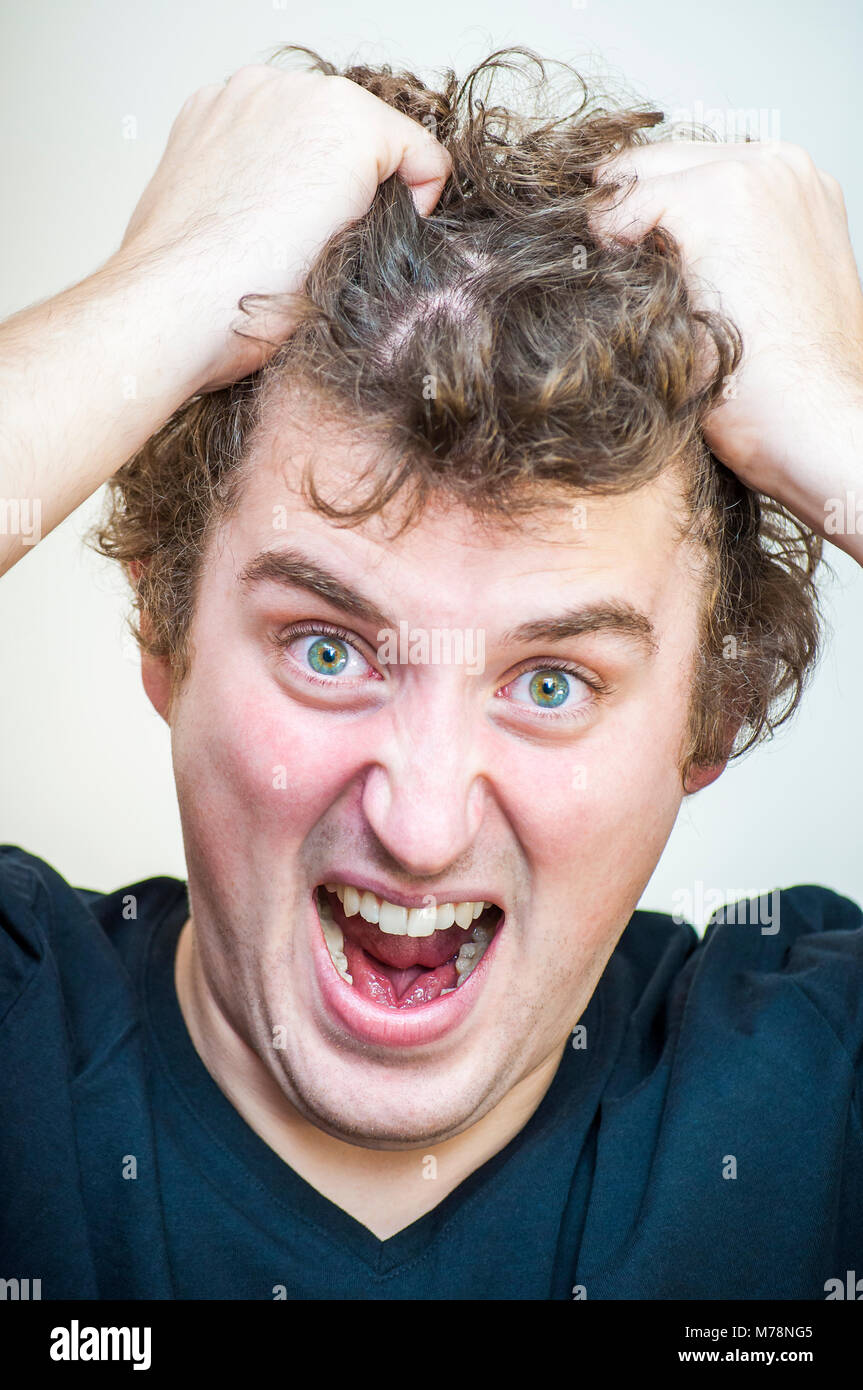 Portrait of young angry screaming curly man tears his hair out on white background. Stock Photo