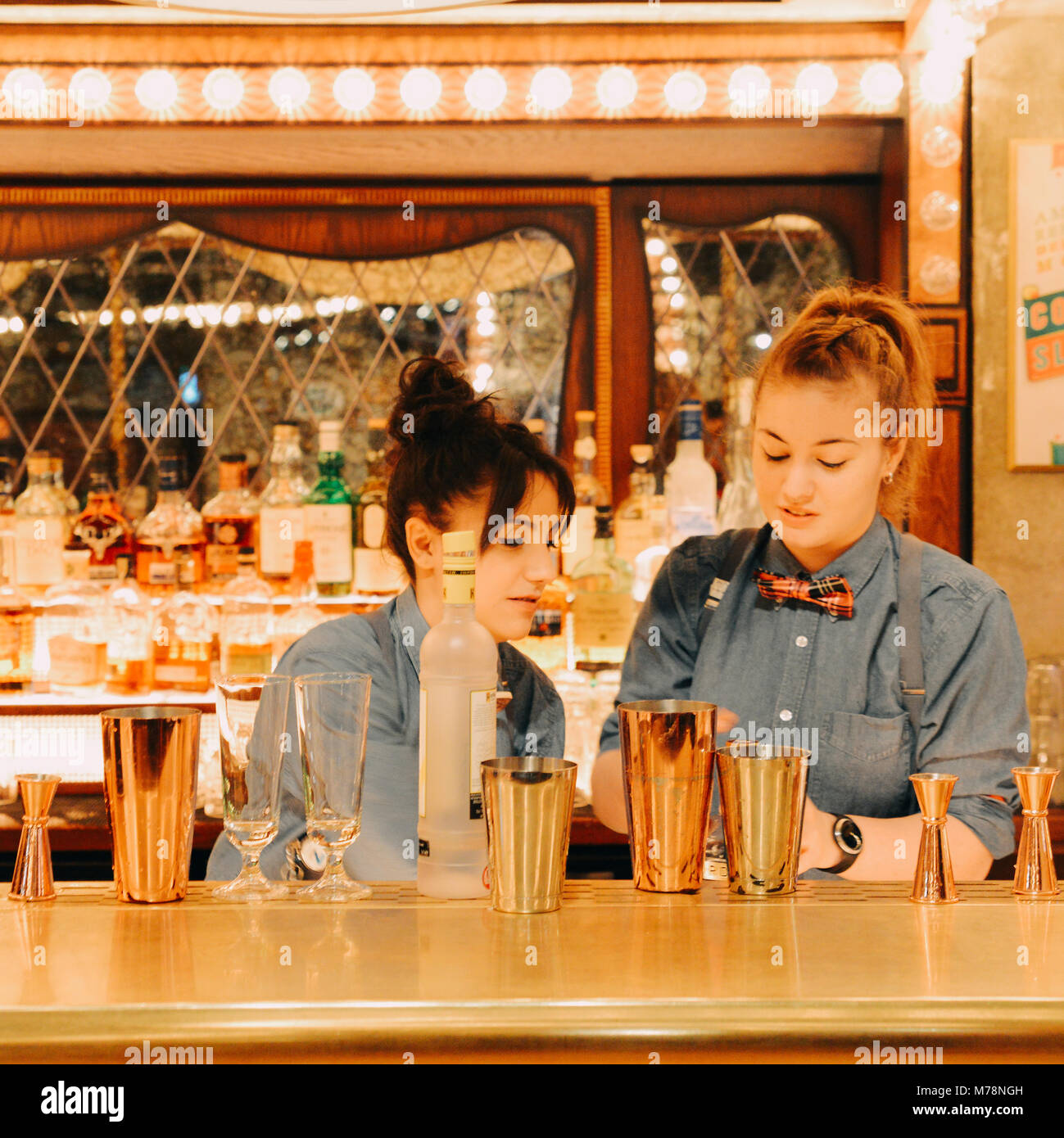Two female bartenders mix drinks at a bright carnival fair style bar counter at the Flight Cub, a vintage social digital darts club in Bloomsbury Stock Photo