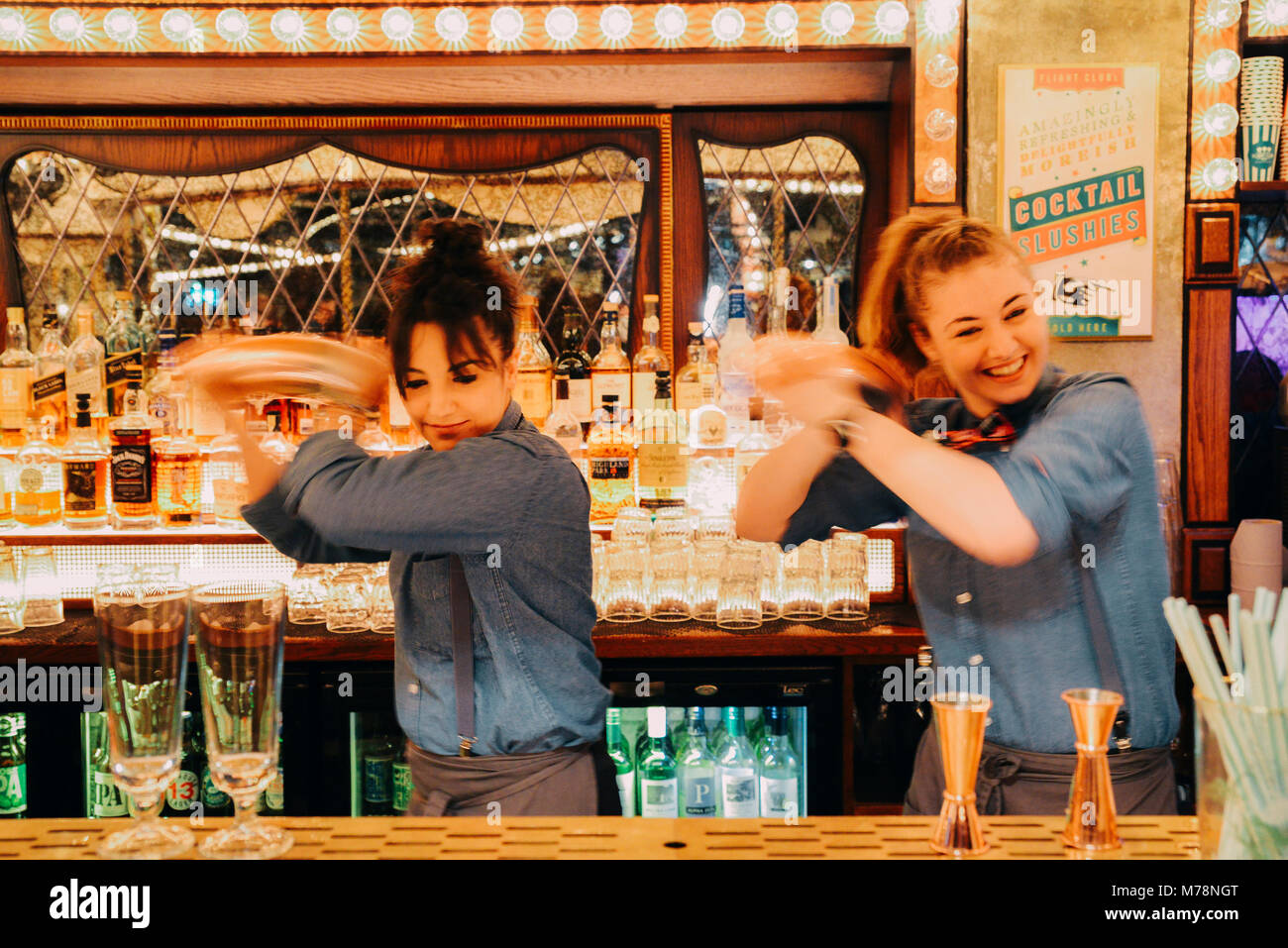 Two female bartenders mix drinks at a bright carnival fair style bar counter at the Flight Cub, a vintage social digital darts club in Bloomsbury Stock Photo