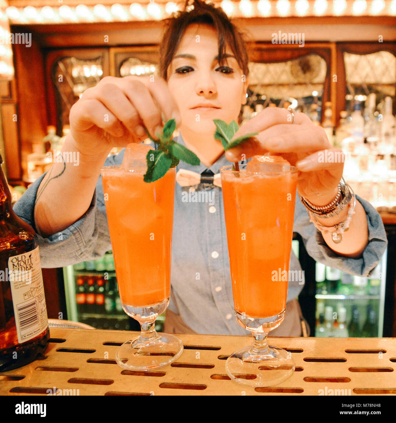 Female bartender prepares a cocktail drink with mint at a bright carnival fair style bar counter at the Flight Cub, a darts club in Bloomsbury, London Stock Photo