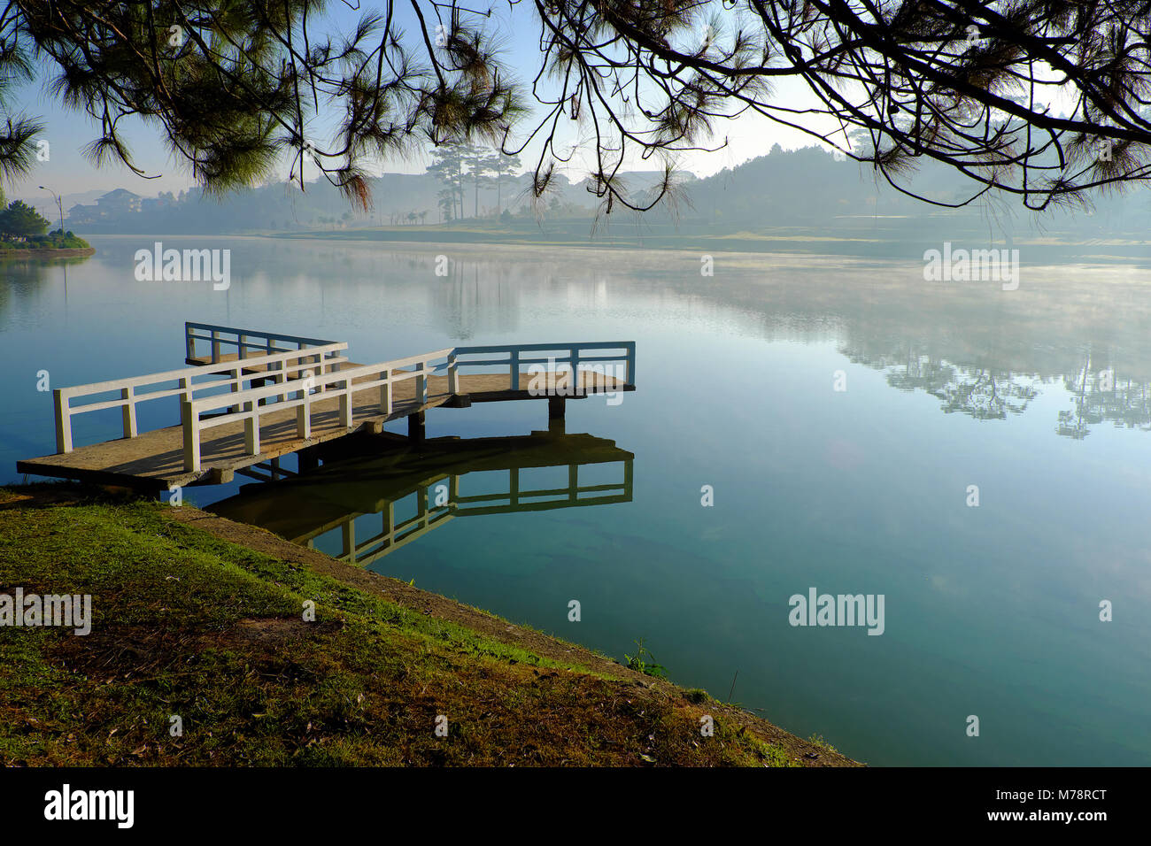 Destination for Vietnam travel at Da Lat city, mist evaporate from surface water of lake, silhouette of small bridge reflect on pond, nice at sunrise Stock Photo