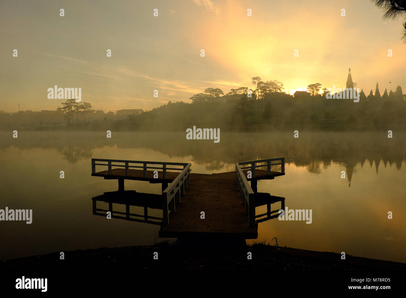 Destination for Vietnam travel at Da Lat city, mist evaporate from surface water of lake, silhouette of small bridge reflect on pond, nice at sunrise Stock Photo