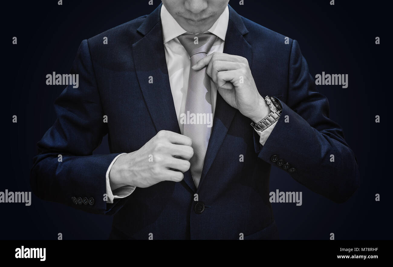 Businessman in dark blue suit tying grey necktie on blue background, vignette Stock Photo