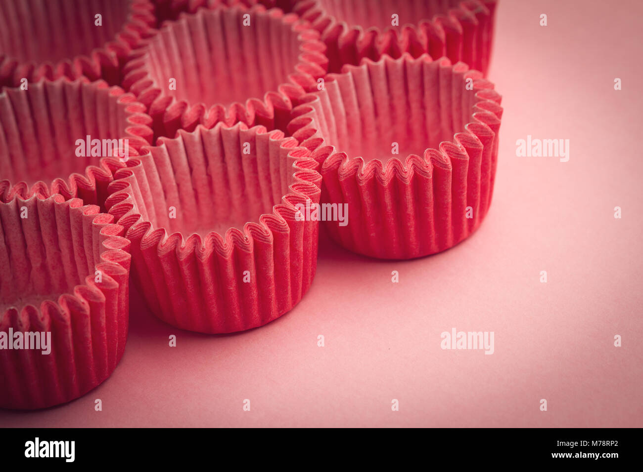 horizontal closeup top view of small paper baking tray holders for cupcakes and muffin on pink background Stock Photo