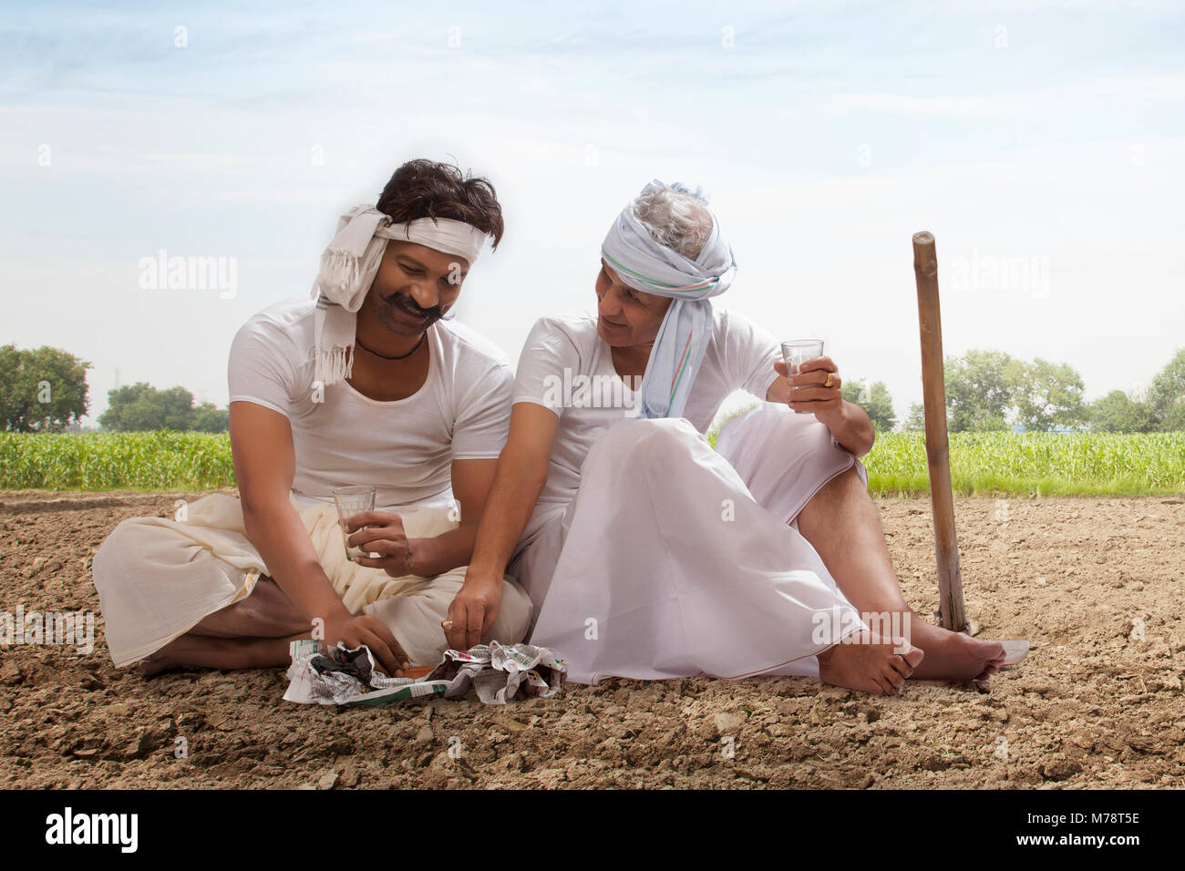 Two farmers sitting in field drinking tea and eating snacks Stock Photo