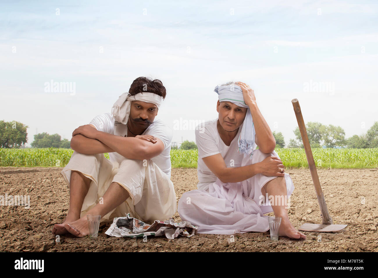 Tensed two farmers sitting in field drinking tea and eating snacks Stock Photo