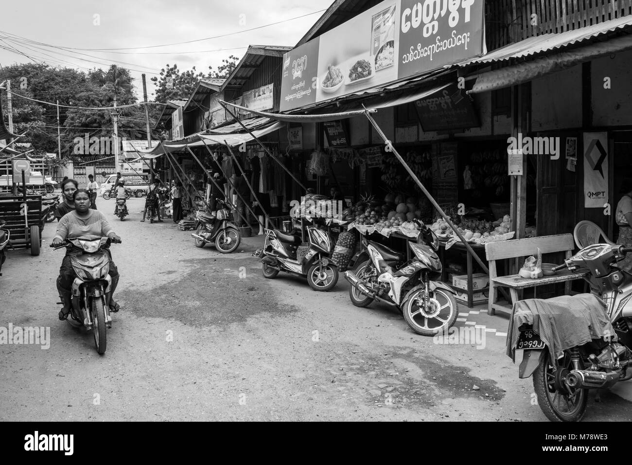 Two Burmese women on one motorcycle bike driving in Nyaun U local outdoor market next to fruit and vegetables, Bagan Myanmar Burma South East Asia Stock Photo